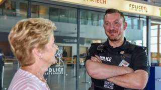 Ein Polizeibeamter spricht mit einer Frau im Innern des Flughafens