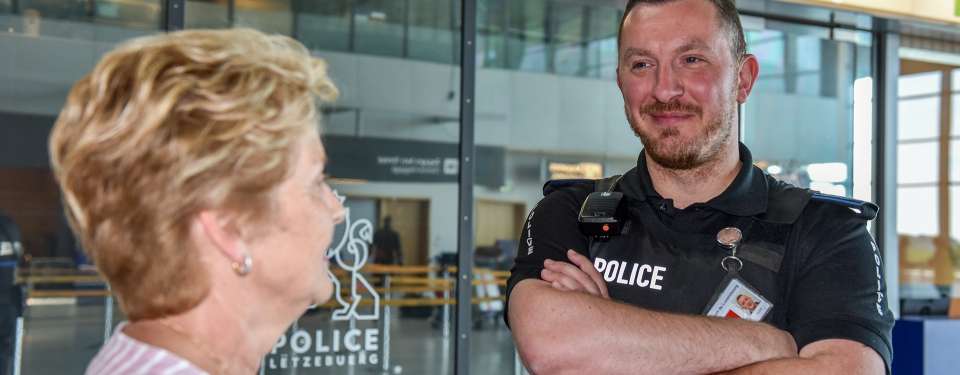 policier devant commissariat à l’aéroport, passagère en avant plan